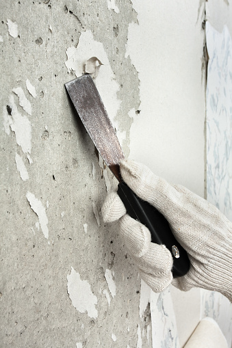 hand in glove removing wallpaper from wall with spatula